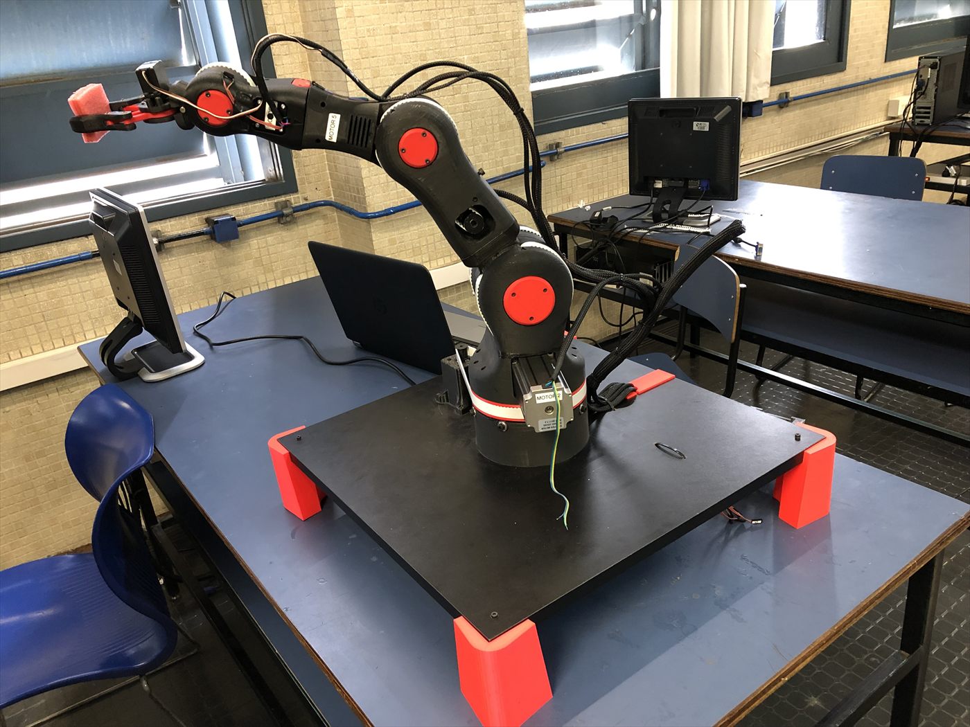 El brazo robótico montado sobre una mesa de trabajo, con sus articulaciones rojas y la base impresa.