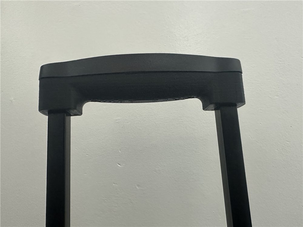 Manija de valija impresa en 3D en negro, con el agarre curvo y dos patas.