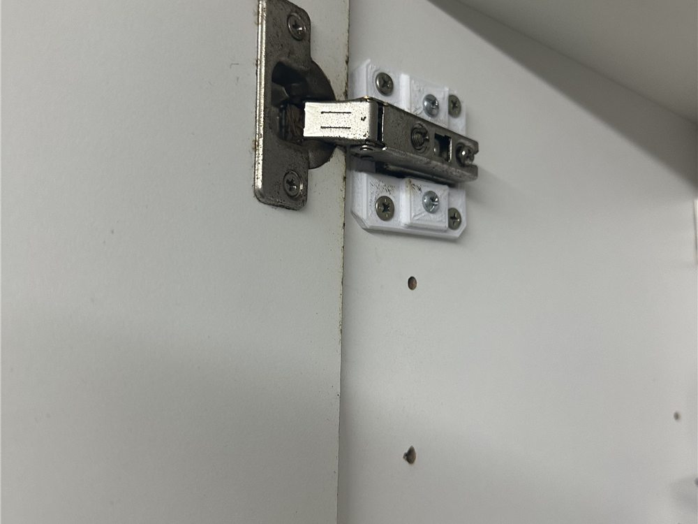 Base blanca impresa en 3D que sostiene una bisagra metálica de mueble, instalada dentro de un placard.