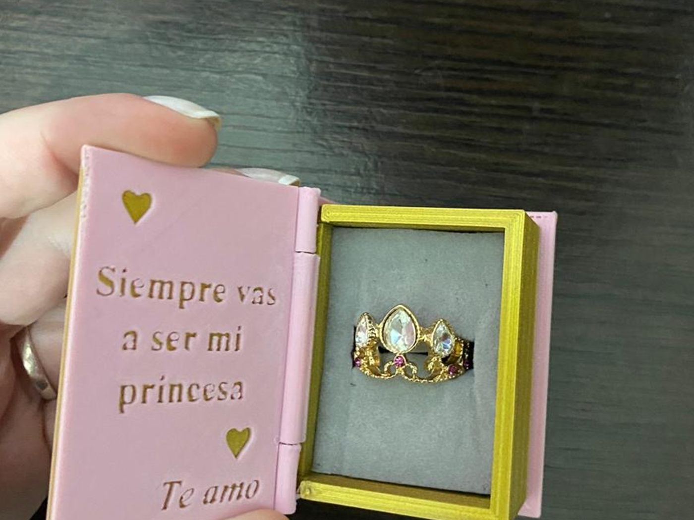 La caja sostenida en la mano, abierta y con un anillo adentro.